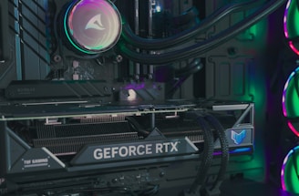 The image depicts the inside of a computer case featuring a high-performance graphics card labeled 'GEFORCE RTX' with RGB lighting. The cooling fans are illuminated with vibrant colors, creating a visually striking look. Various cables and components are neatly arranged, highlighting advanced hardware and a focus on aesthetics.